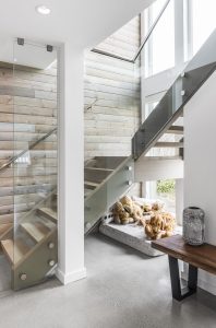 a cute dog in a bed under a set of stairs with glass railings