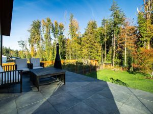 Deck with grey tile and glass railings overlooking a beautiful yard.