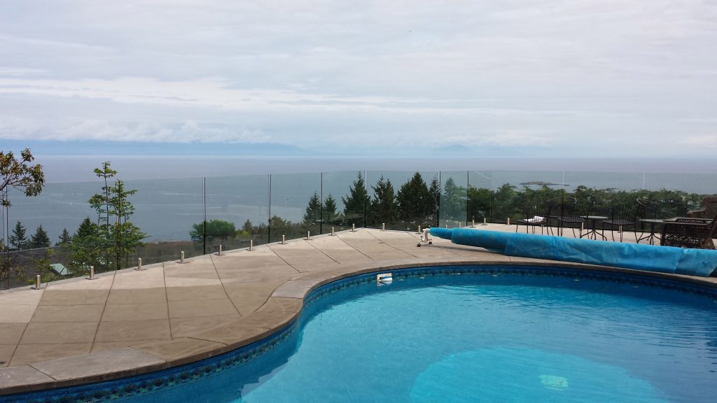 Photo of a pool surrounded by a frameless glass railing overlooking the ocean