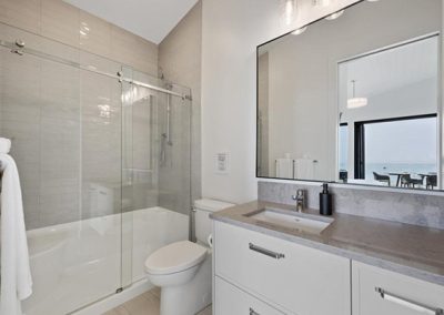 High end white bathroom with frameless sliding glass shower door and grey countertops.